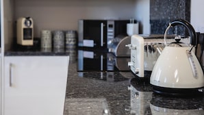 A kitchen with a white kettle, a toaster, and a coffee maker on the counter. - Harbour Lights House (Seahouses)