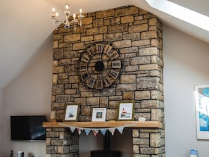 A stone fireplace with a large clock, framed pictures, and a TV above it. - Harbour Lights House (Seahouses)