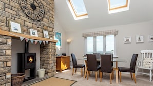 A cozy room with a stone fireplace, a dining table with chairs, and a large window with a view. - Harbour Lights House (Seahouses)