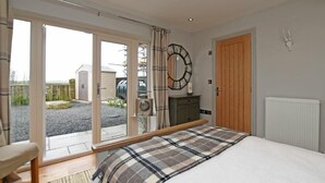 A bedroom with a bed, a wooden bench, a large window, and a view of the outside. - The Hemmel (Chathill)
