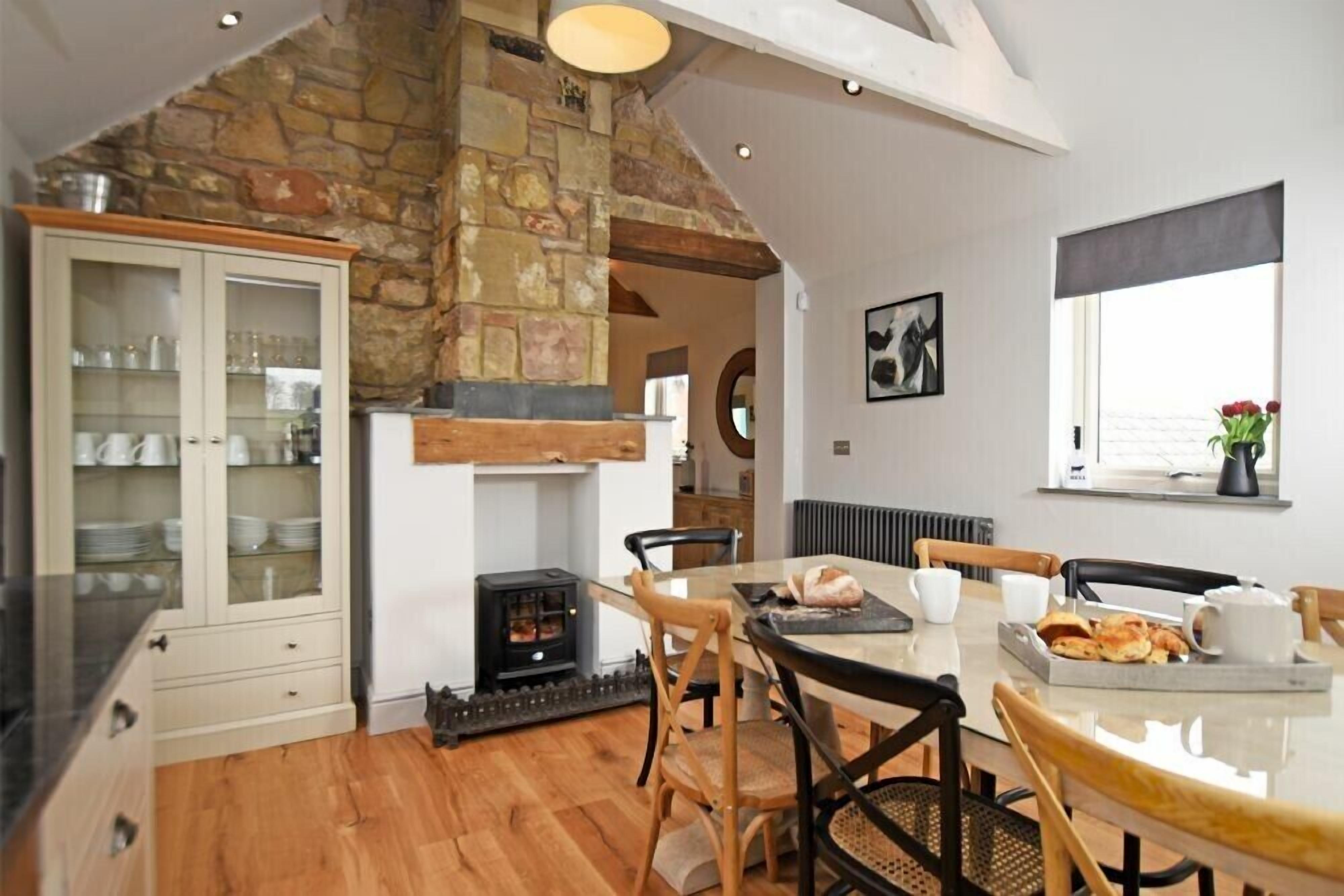 Una cocina acogedora con pared de piedra, vigas de madera y comedor con mesa dispuesta para cuatro.