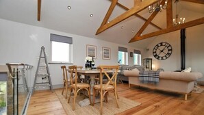 A spacious living area with a wooden dining table, chairs, a sofa, and a large clock on the wall. - The Hemmel (Chathill)