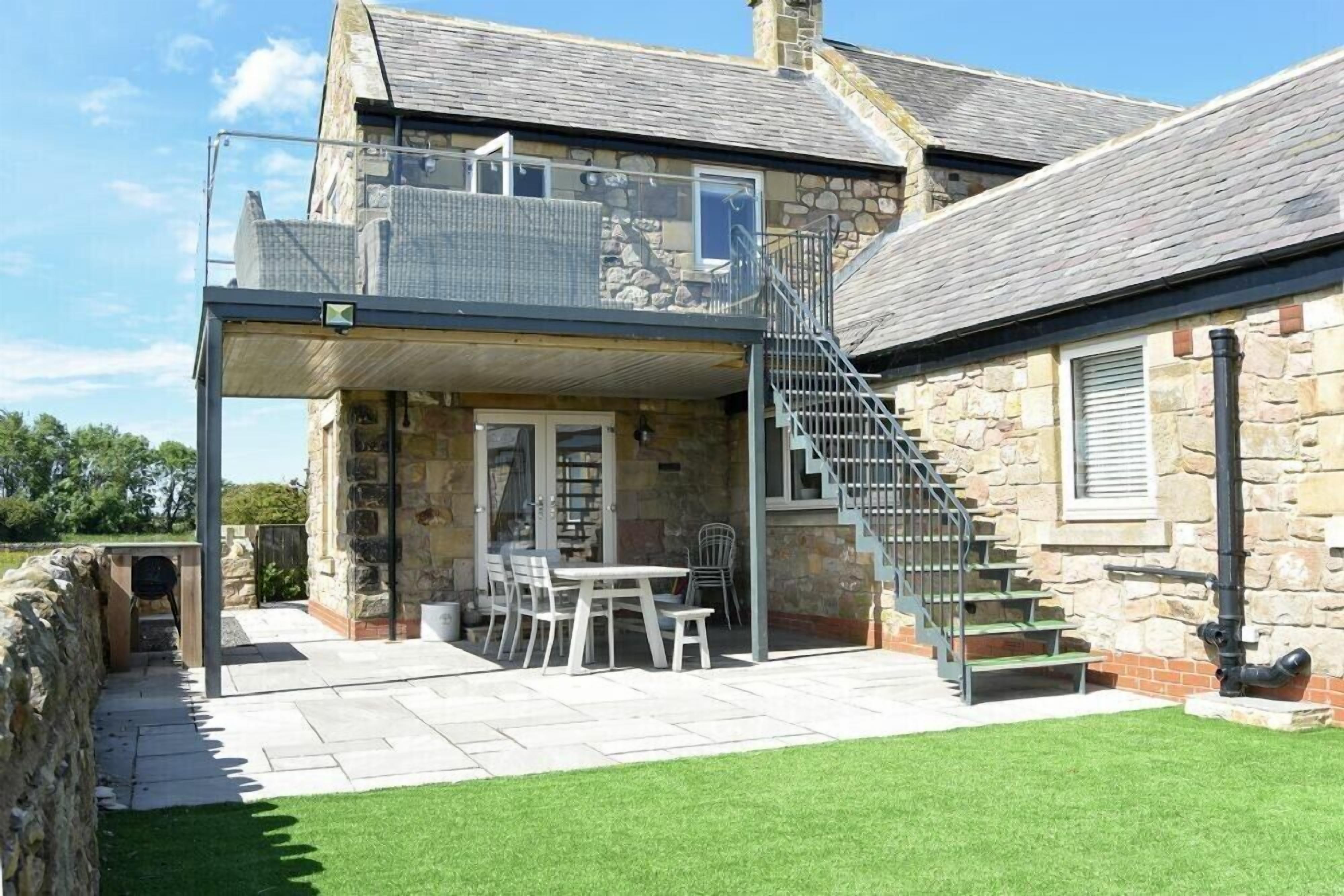 Une maison en pierre dotée d’un balcon, d’un escalier et d’une terrasse aménagée avec du mobilier d’extérieur.
