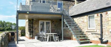 Une maison en pierre dotée d’un balcon, d’un escalier et d’une terrasse aménagée avec du mobilier d’extérieur.