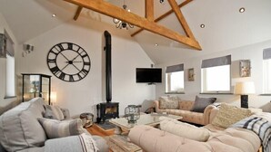 A spacious living room with a large clock, a fireplace, and comfortable seating. - The Hemmel (Chathill)