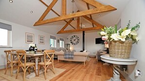 A spacious living area with a wooden dining table and chairs, a sofa, and a large clock on the wall. - The Hemmel (Chathill)