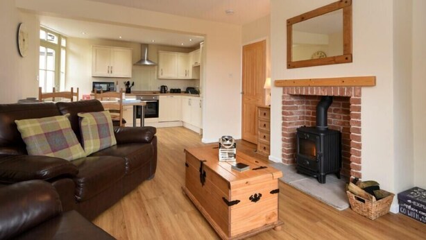 A cozy living room with a brown leather sofa, a wooden chest, and a fireplace.