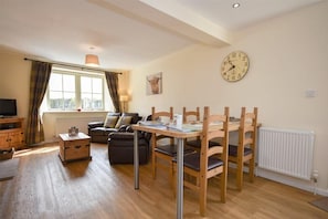 Un salon chaleureux avec un canapé, une table à manger en bois et des chaises, une horloge au mur et une fenêtre avec des rideaux.