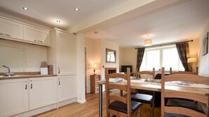 A modern kitchen with white cabinets, a wooden dining table with chairs, and a window with curtains.