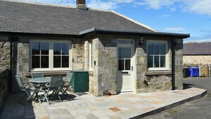 A stone building with a tiled patio, a chimney, and a door.