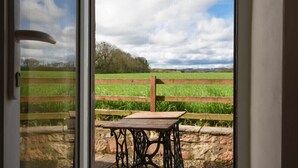 A view through a glass door of a rural landscape with a wooden table and a stone wall. - Dunrovin (Chathill)