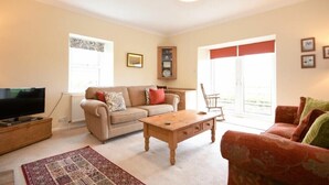 A living room with a sofa, a coffee table, a TV on a stand, and a patterned rug. - Dunrovin (Chathill)