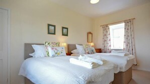 A double room with two beds, each with white bedding and floral pillows. There are two framed pictures on the wall, a mirror above the left bed, and a window with floral curtains. - Dunrovin (Chathill)