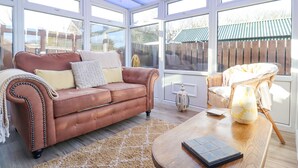 A sunroom with a brown leather sofa, a wicker chair, and a wooden coffee table. - The Bolthole (Seahouses)