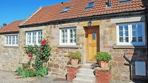 A stone building with a tiled roof, a wooden door, and white-framed windows. - Martins Cottage (Alnwick)