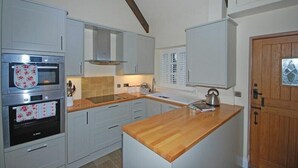 A kitchen with white cabinets, a wooden countertop, a built-in oven, and a skylight. - Martins Cottage (Alnwick)