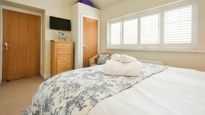 A bedroom with a bed, a dresser, a television, and a window with blinds. - Martins Cottage (Alnwick)