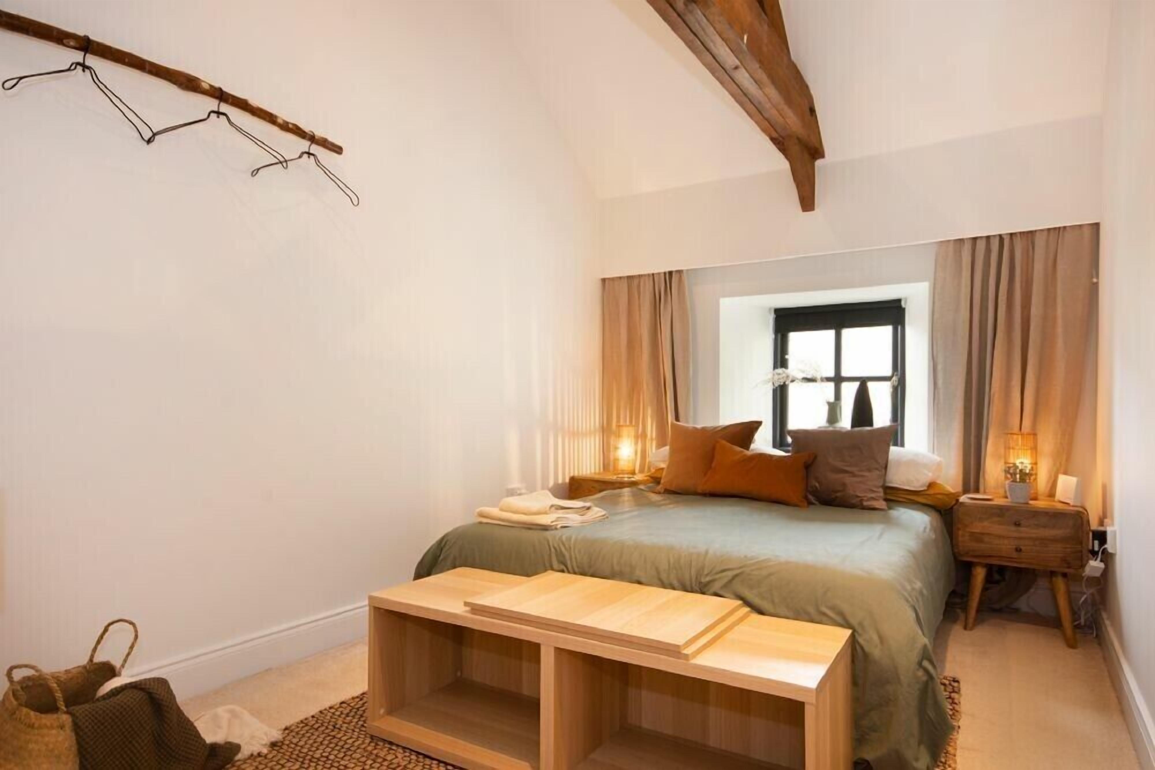 A bedroom with a bed, bedside tables, a wooden bench, a window, and a hanging rack.