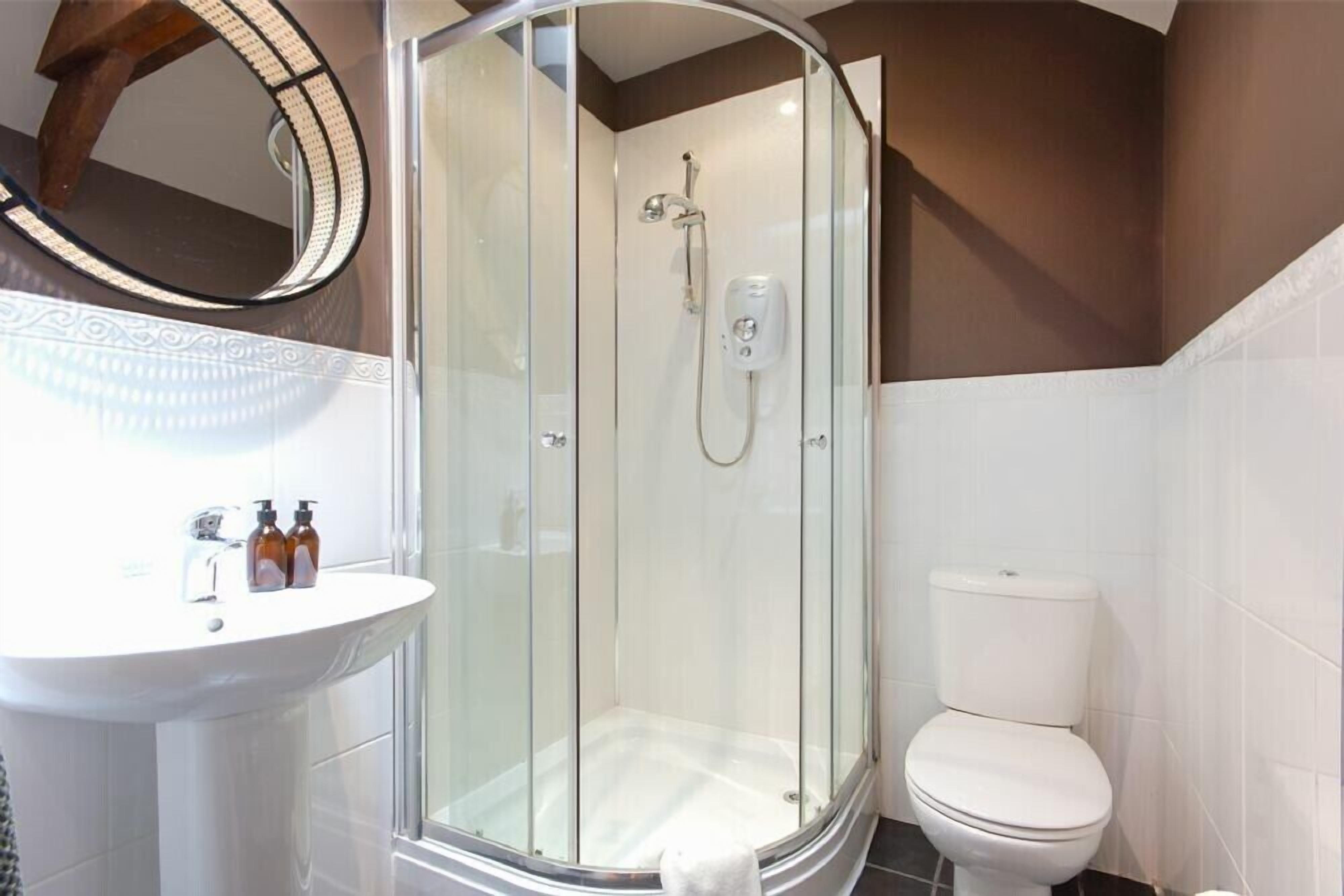 Une salle de bain moderne avec une douche à parois de verre, un lavabo blanc doté de distributeurs de savon et des toilettes.