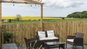 A wooden deck with wicker furniture, a pergola, and a view of a field with horses.