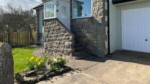 A stone house with a white garage door, a small front porch, and a garden with yellow flowers.