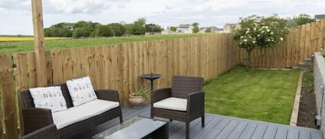 An outdoor deck with wicker furniture, a small table, and a potted plant.