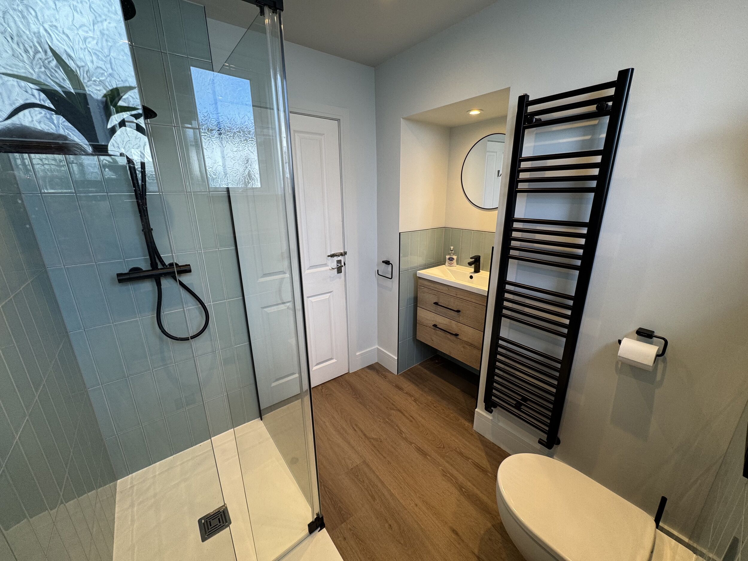 A bathroom with a glass shower enclosure, a toilet, a sink with a mirror, and a towel rack.