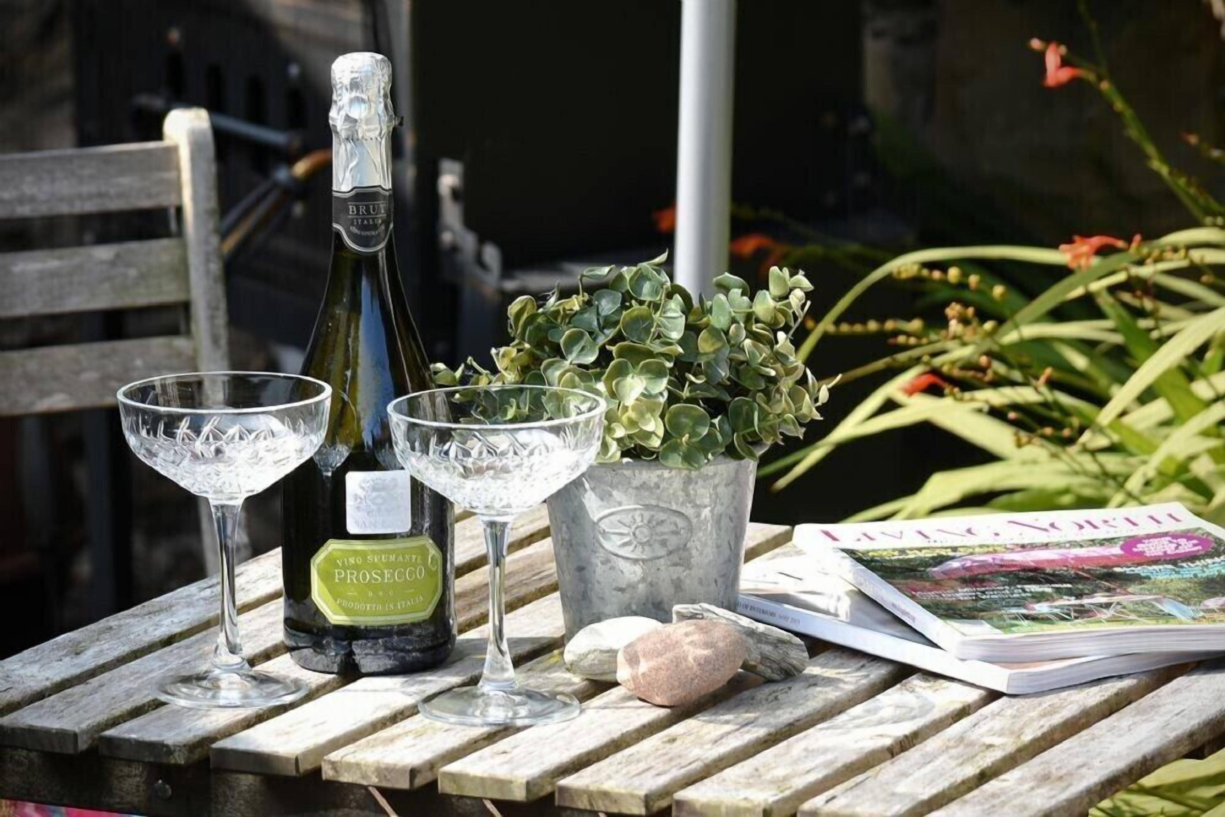 A table with a bottle of wine, two glasses, a potted plant, and a magazine.