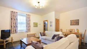 A living room with a sofa, a coffee table, a TV, and a dining area with a table and chairs. - Crier Cottage (Alnwick)