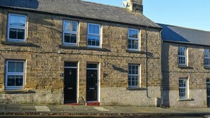 A stone building with multiple windows and doors, featuring a traditional architectural style. - Crier Cottage (Alnwick)