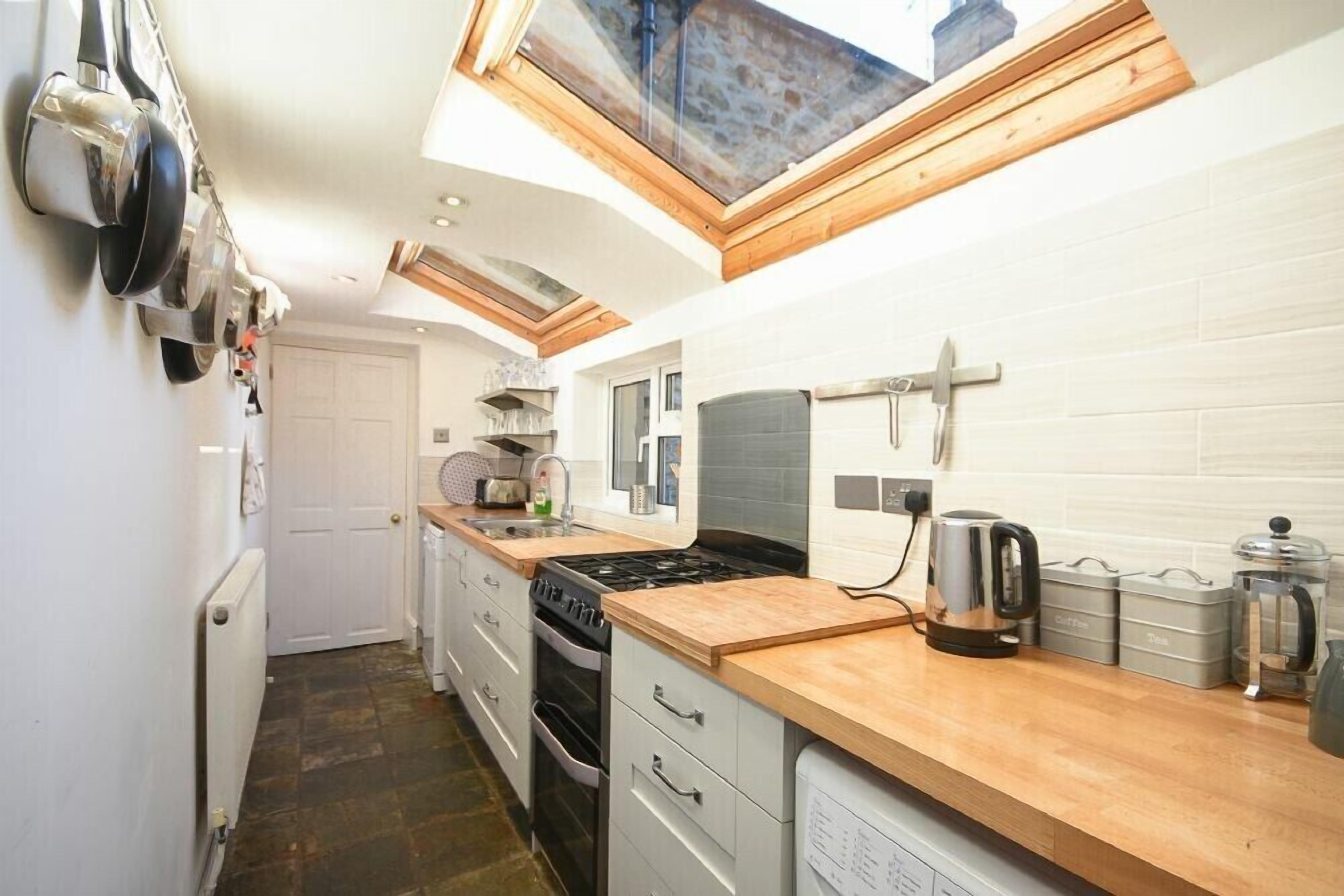 Una cocina funcional con tragaluz, paredes de azulejos blancos, encimera de madera y electrodomésticos de acero inoxidable.
