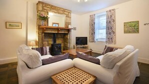 A living room with a stone fireplace, a television, two white sofas, and a wooden coffee table. - Crier Cottage (Alnwick)