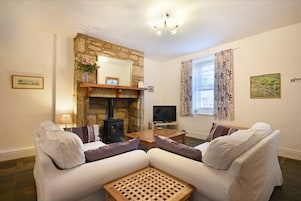 A living room with a stone fireplace, a television, two white sofas, and a wooden coffee table.