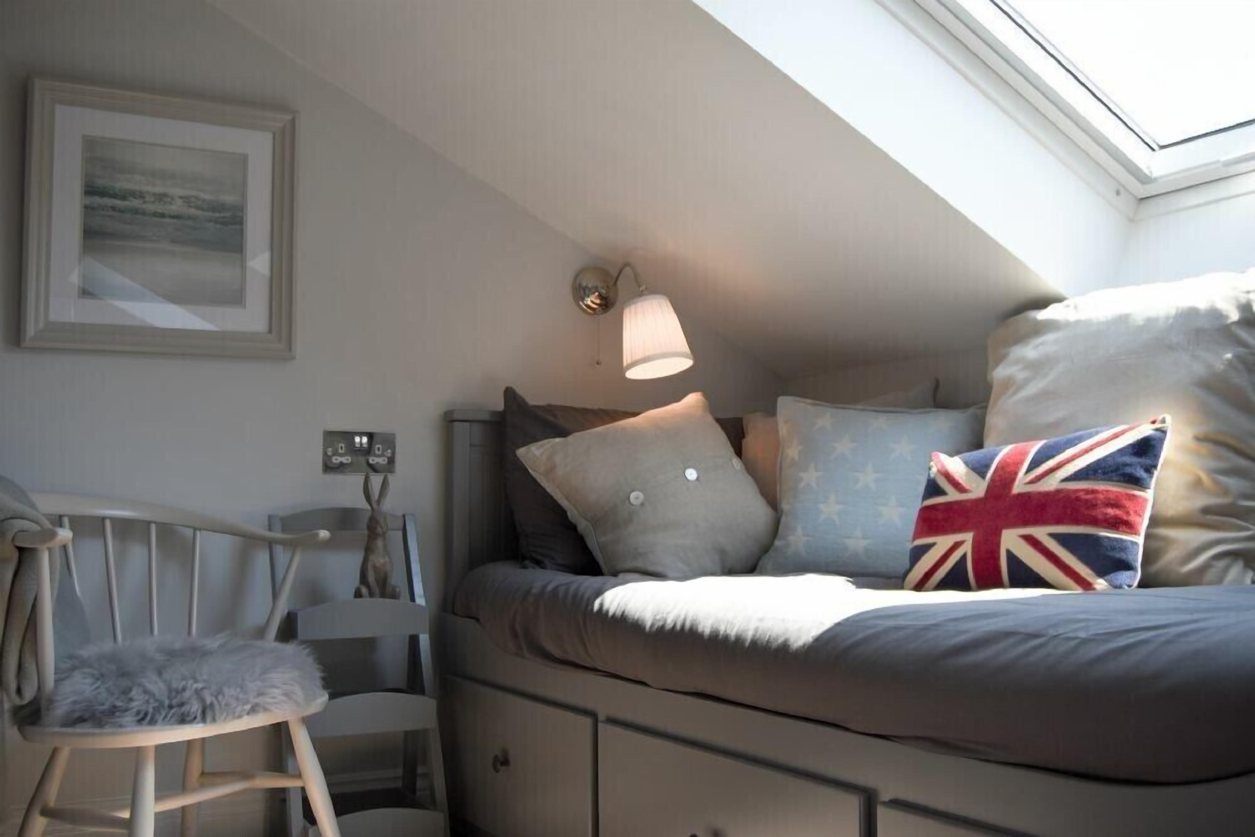 Un dormitorio acogedor con cama, una silla, una lámpara de pared y un cuadro enmarcado.
