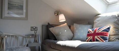 Un dormitorio acogedor con cama, una silla, una lámpara de pared y un cuadro enmarcado.