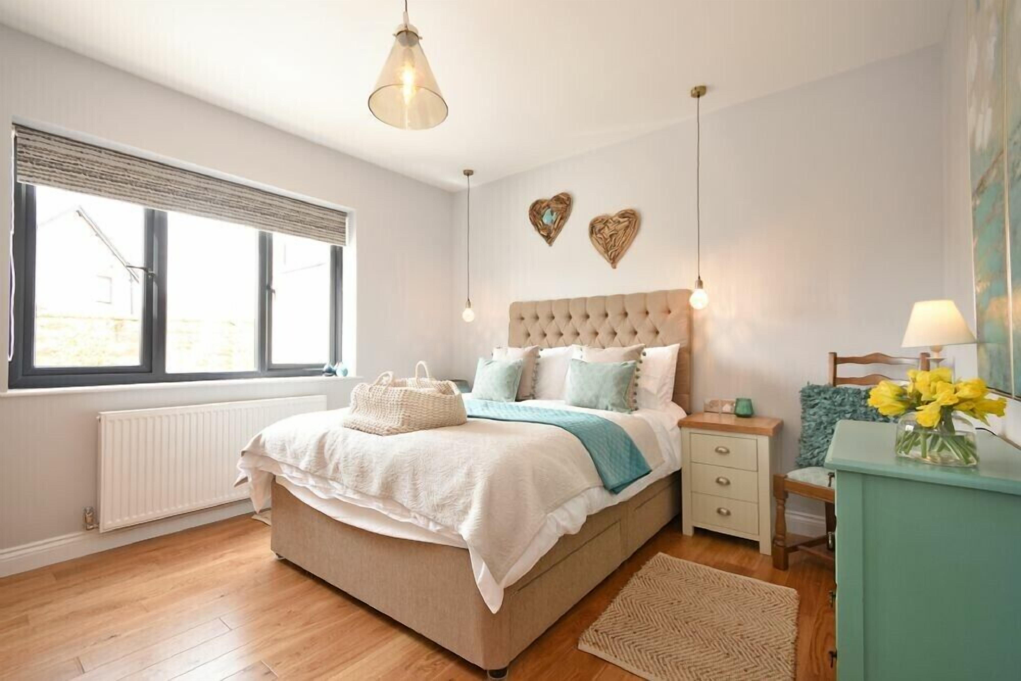 A bedroom with a large bed, bedside tables, a dresser, and a window with blinds.