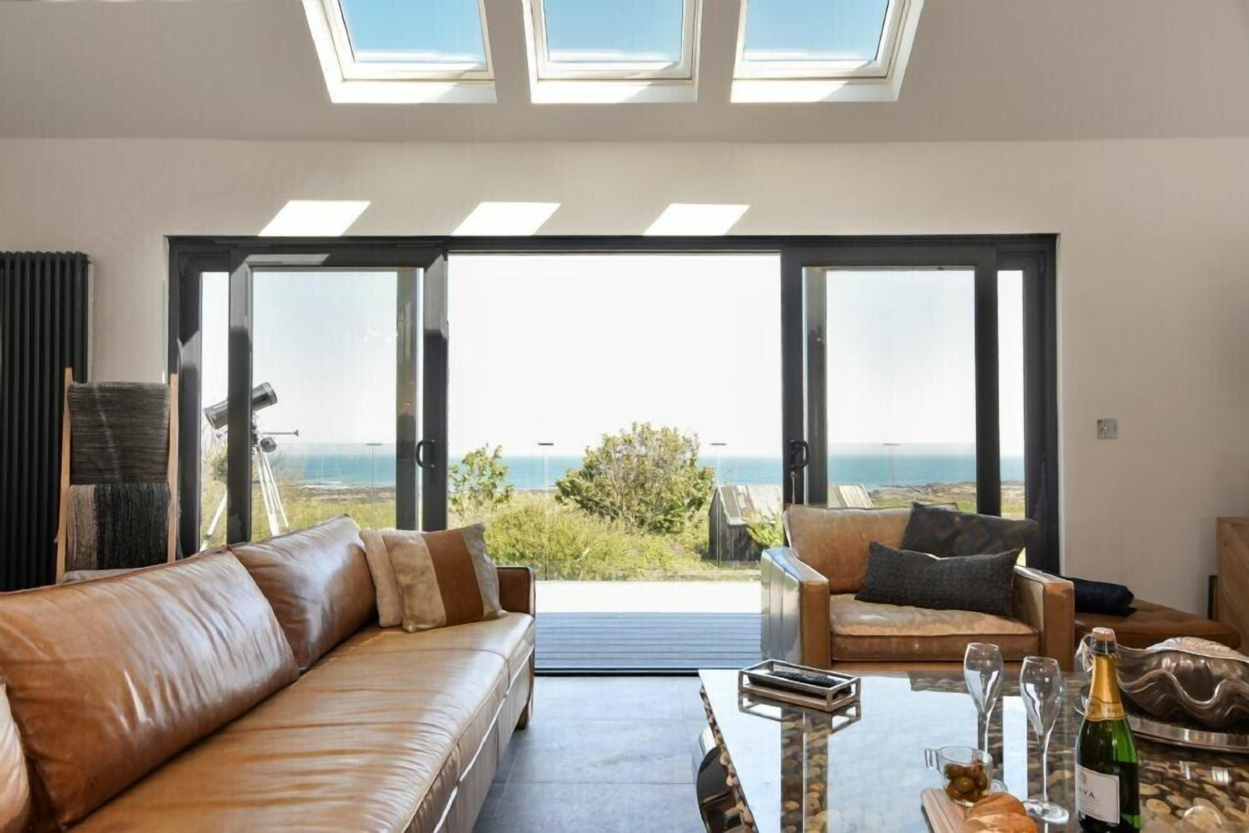 A modern living room with a leather sofa and armchair, a coffee table, and a view of the ocean through large glass doors.