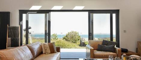 A modern living room with a leather sofa and armchair, a coffee table, and a view of the ocean through large glass doors.