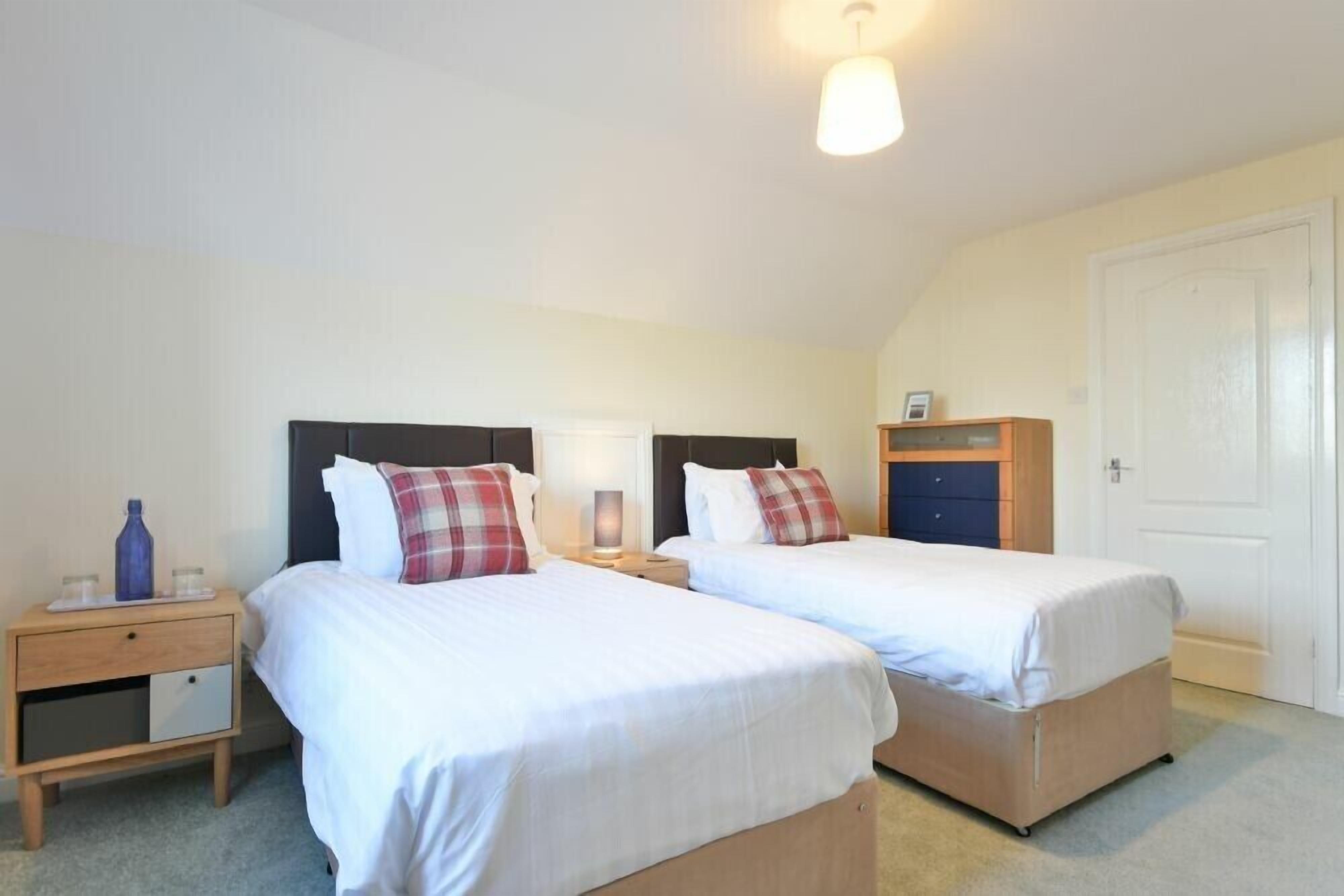 Une chambre à deux lits, comprenant deux lits simples, une table de chevet, une commode et un luminaire au plafond.