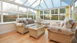 A conservatory with wicker furniture, large windows, and a ceiling fan. - Annstead House (Seahouses)