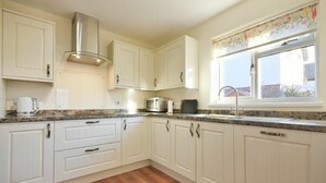 A kitchen with white cabinets, a stainless steel range hood, a microwave, and a window with a floral curtain. - Annstead House (Seahouses)