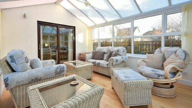 A conservatory with wicker furniture, large windows, and a glass door. - Annstead House (Seahouses)