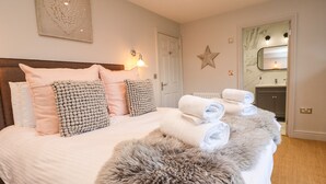 Una cama bien hecha con almohadas mullidas y toallas enrolladas, un adorno con forma de estrella en la pared, y un baño visible a través de una puerta abierta.