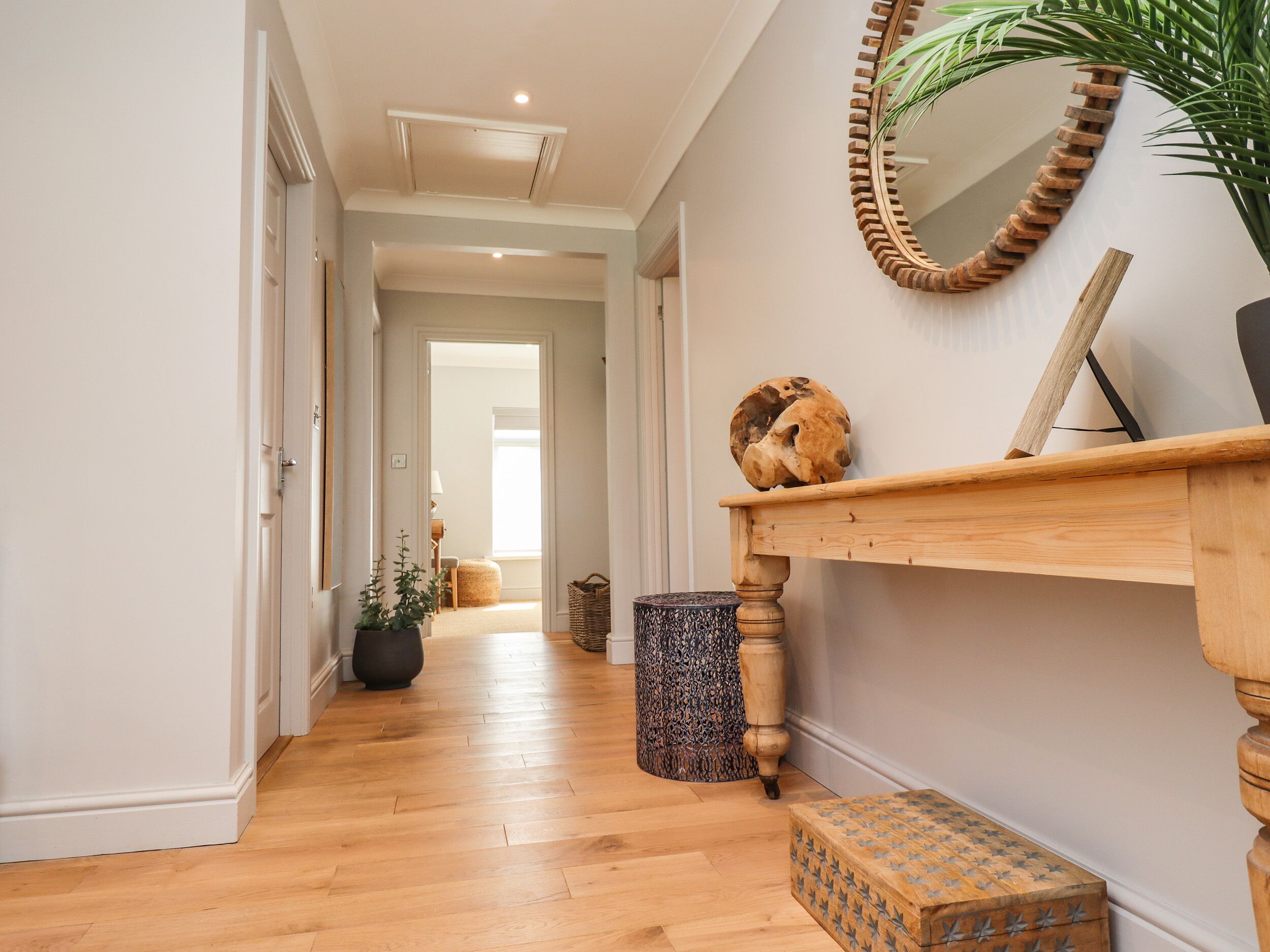 Un couloir doté d’un plancher en bois, une console en bois avec un miroir, une plante en pot et un objet décoratif en bois.
