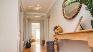 Un pasillo con piso de madera, una consola de madera con un espejo, una planta en maceta y un objeto decorativo de madera.