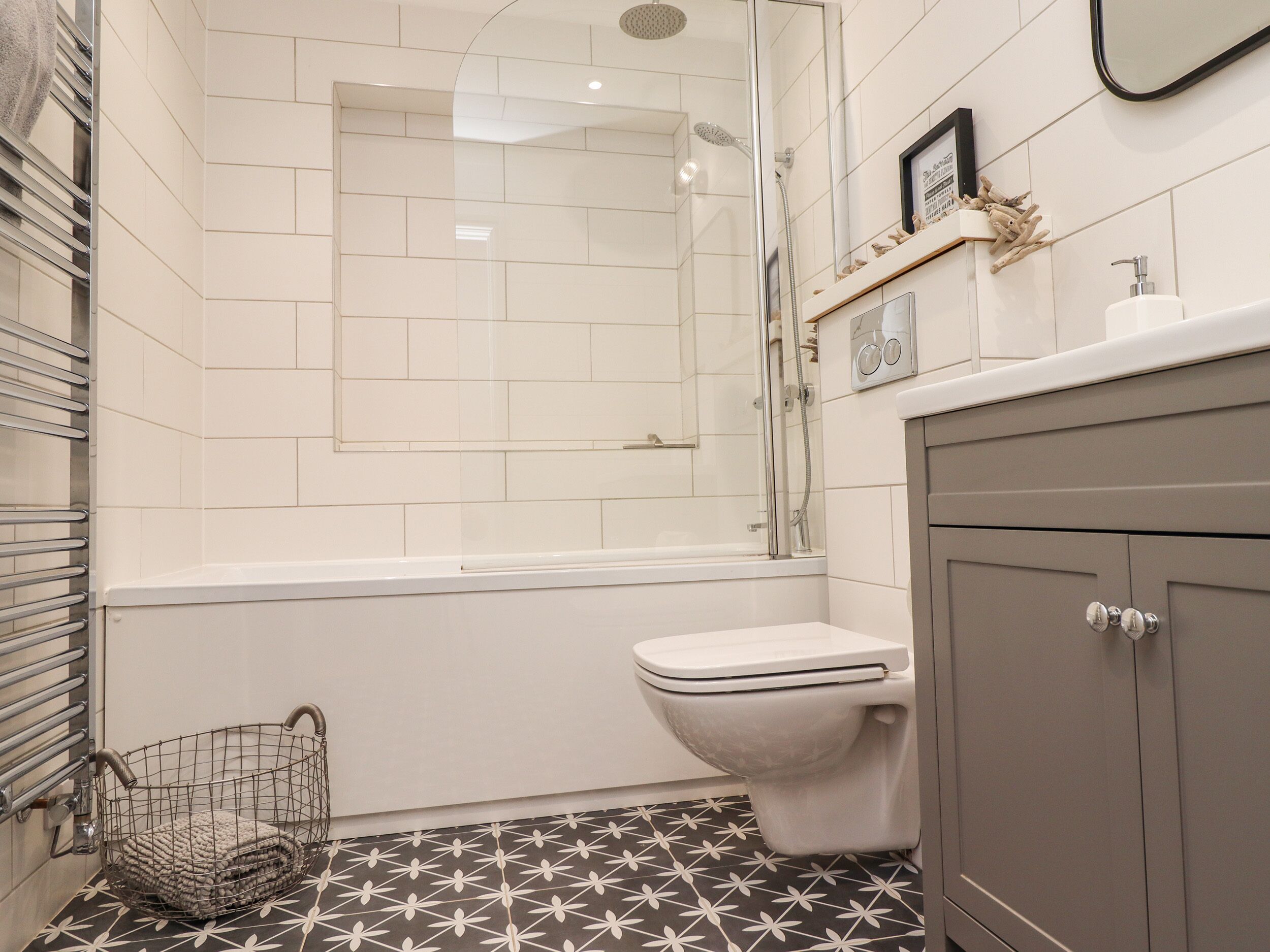 Une salle de bain avec une douche, des toilettes et un panier en métal posé sur le sol.