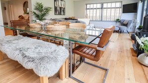 Una sala moderna con una mesa de comedor de vidrio, sillas de cuero y un rincón de estar acogedor con un sofá y sillones.