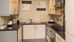 Una cocina moderna con armarios blancos, una encimera negra y dos obras de arte con motivos de pera.