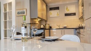 Una cocina moderna con armarios blancos, una mesa de comedor servida con platos y vasos, y una botella de vino.