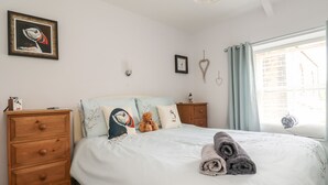 Quarto com cama, cómoda de madeira e um quadro de um pássaro na parede.